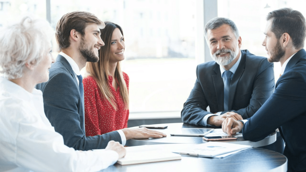 Five smiling business professionals of mixed ages are seated around a conference table.
