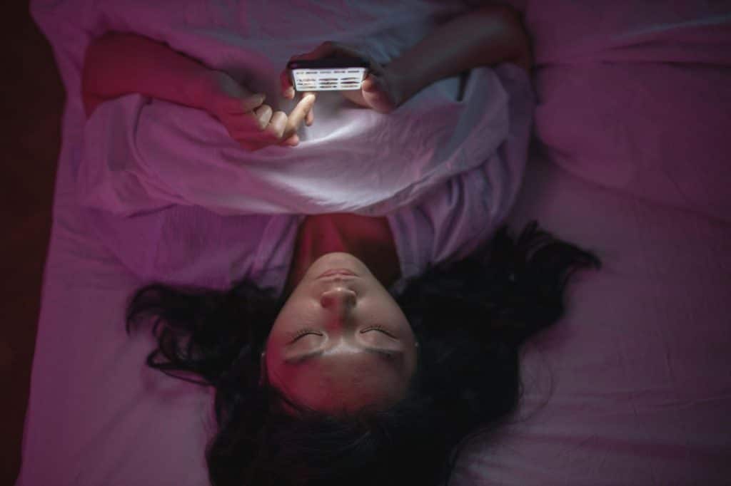 A woman lying on bed while using phone