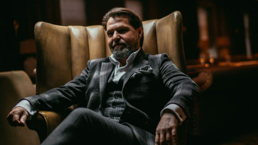 A handsome, well-dressed man sits back and relaxes in a dark leather armchair.