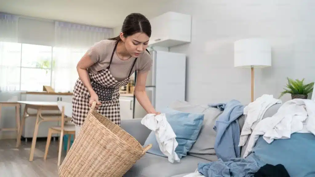 An annoyed woman picking up the dirty clothes of her partner in the living room