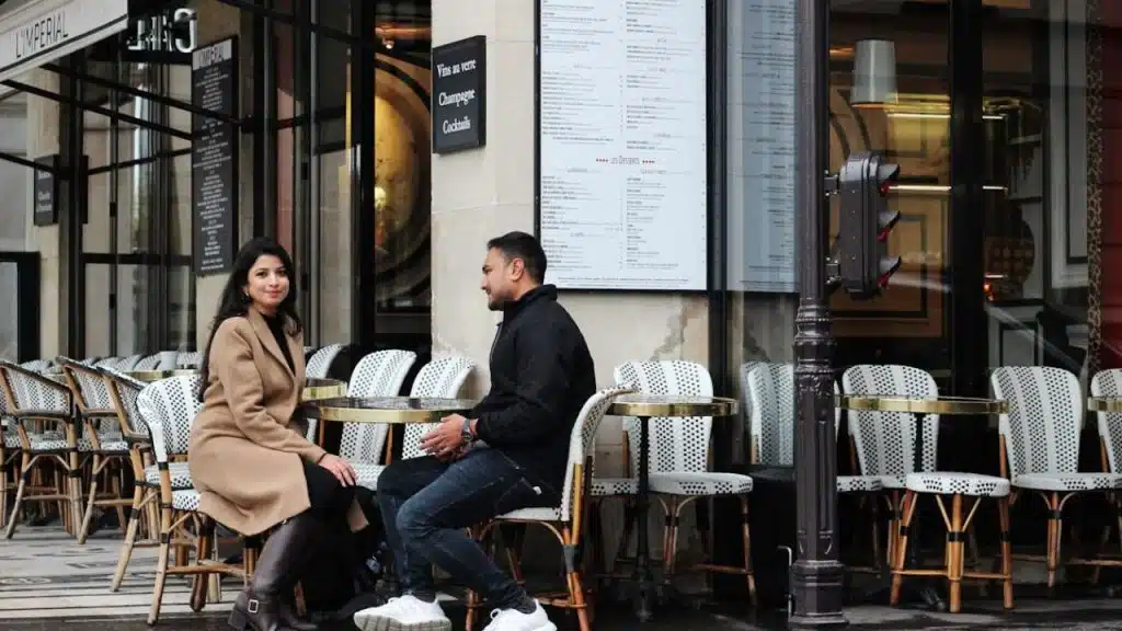 A couple at a café, man smirking sarcastically while the woman looks unimpressed.