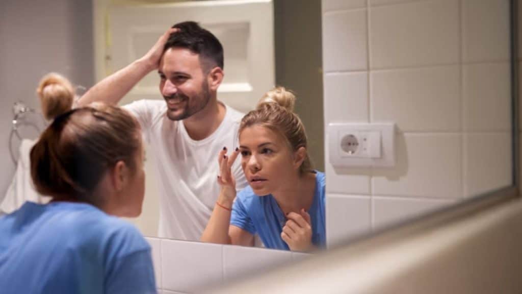 Woman standing near her partner waiting impatiently for her turn to use the mirror