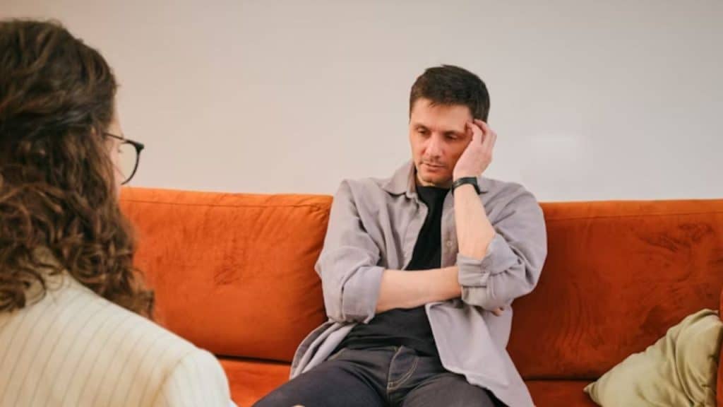 Man sitting on the couch stressed while his partner looks concerned