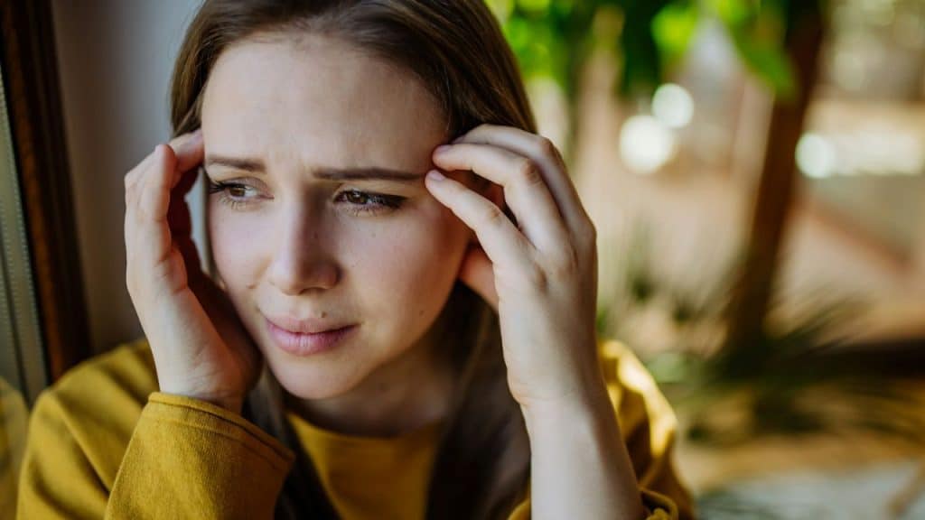 Close-up of a young woman with a concerned expression holding her temples with both hands.