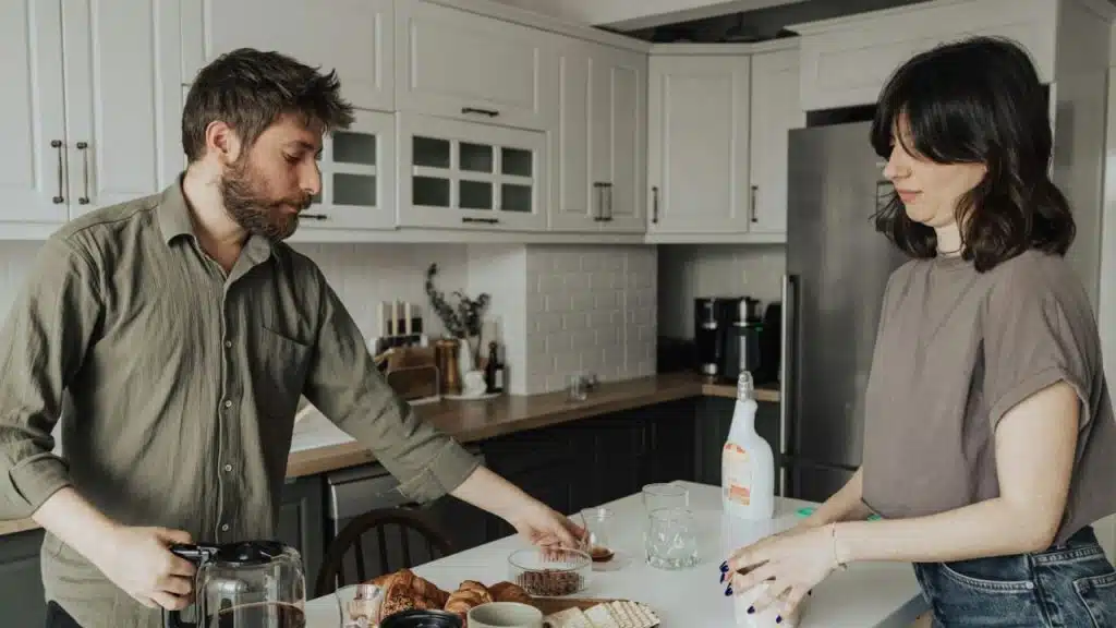 A bearded man and a woman prepare breakfast together in a modern, light-colored kitchen.