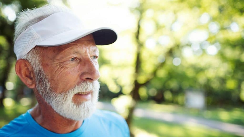 Close-up side profile of a senior man with a white beard and visor outdoors.