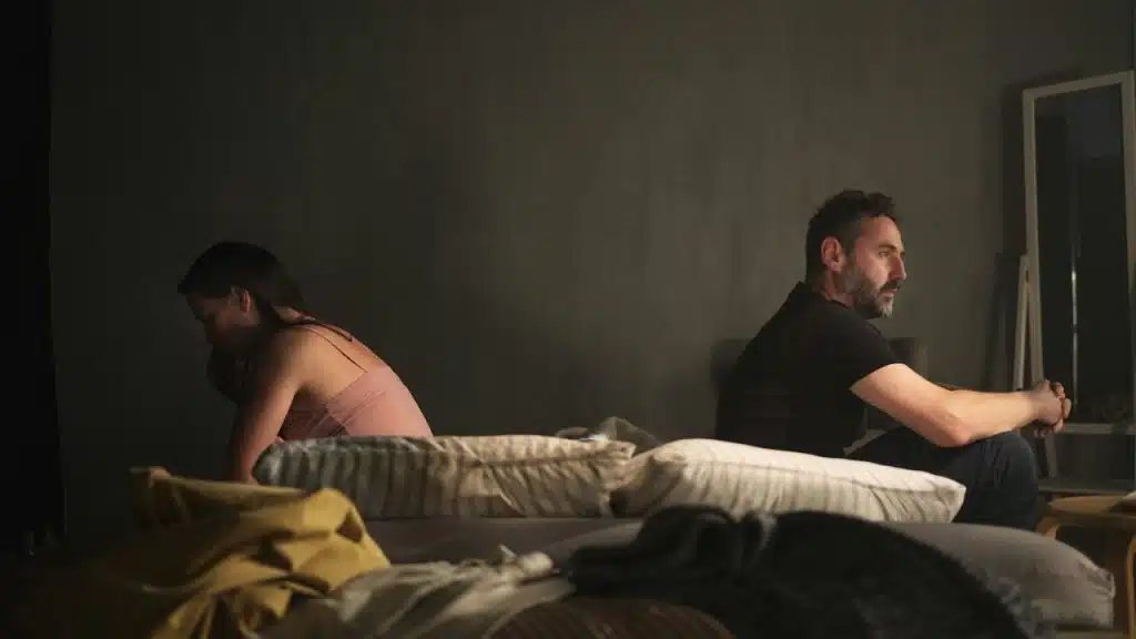 A couple sitting on a bed and facing away from each other.