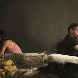 A couple sitting on a bed and facing away from each other.