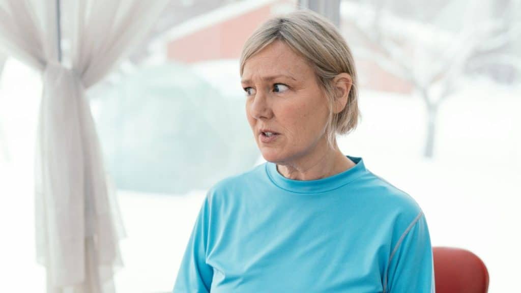 A middle-aged blonde woman in a blue shirt looks away with a surprised or distressed expression.