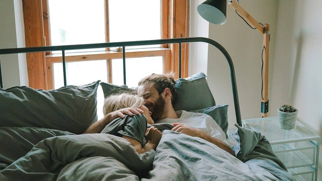 A couple lying in bed with the man kissing his partnerβs forehead.