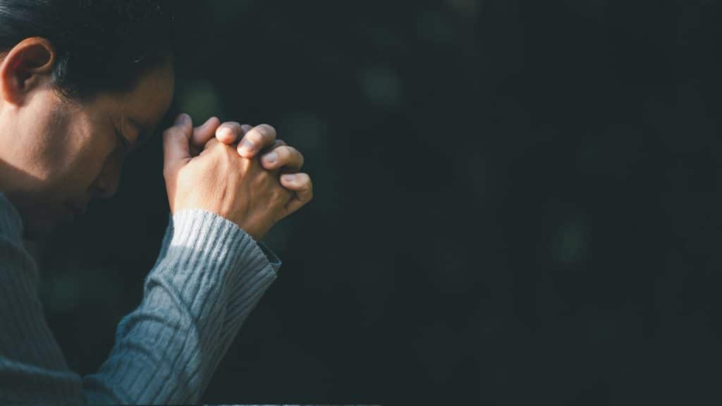 A man holding crossed hands to his forehead and thinking deeply with his eyes closed.