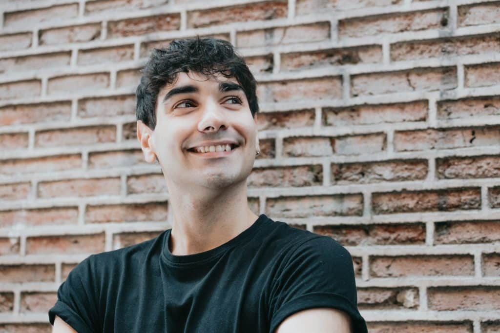 The man standing in front of a brick wall is smiling.