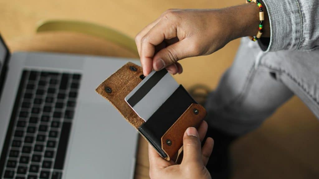 A person holding a wallet and taking out a credit card near a laptop.