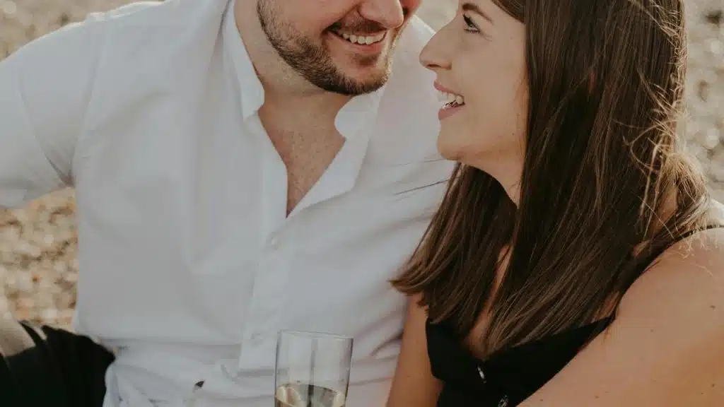 A couple smiling at each other while sitting outdoors with a drink.