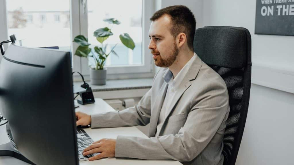 Man in a light grey suit sitting at a desk and working on a computer.