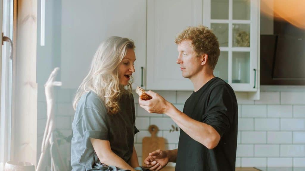 A man feeding a woman a piece of food in a kitchen.