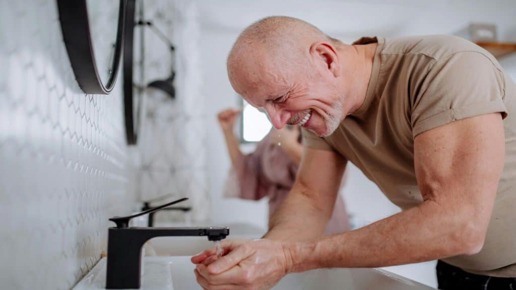 A mature man laughing while doing skincare