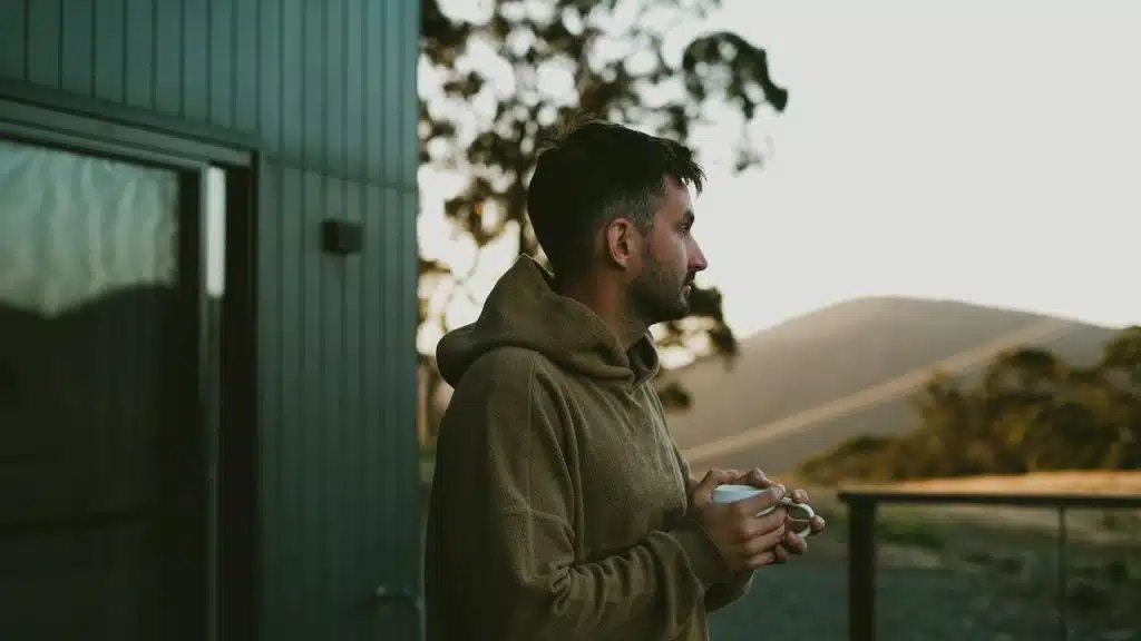 A man in a hoodie standing outside holding a cup and looking at the scenery.