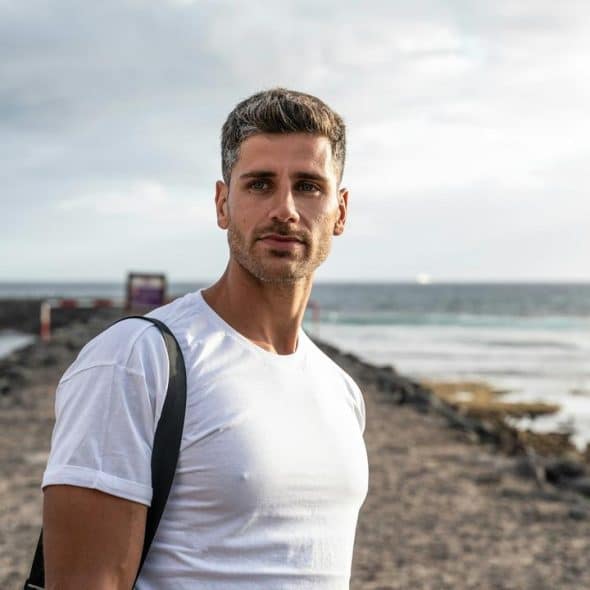 A man in a white t-shirt standing by the ocean.