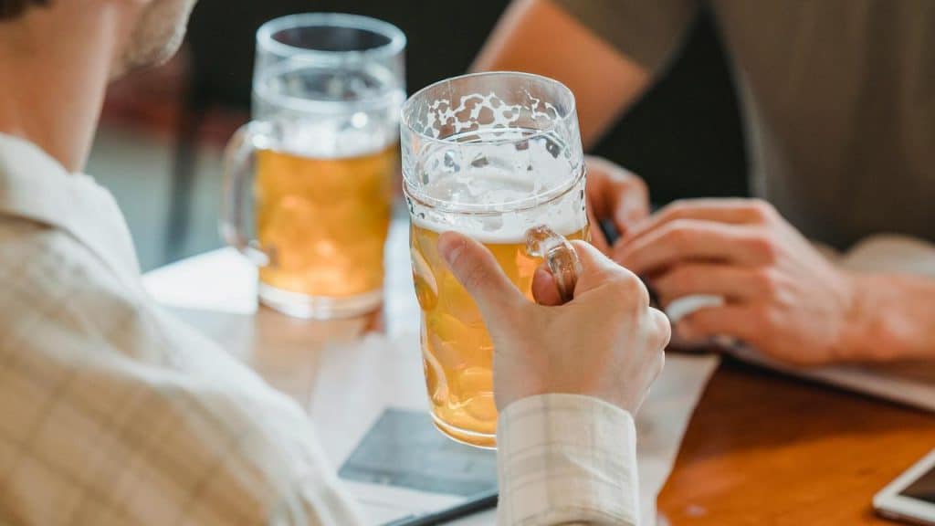 A close-up of two people holding large glasses of beer at a table.