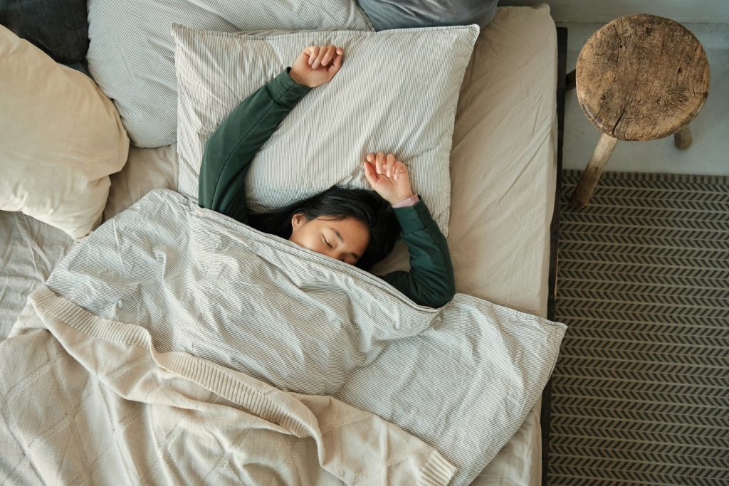 The woman is lying in the bed under the blanket.