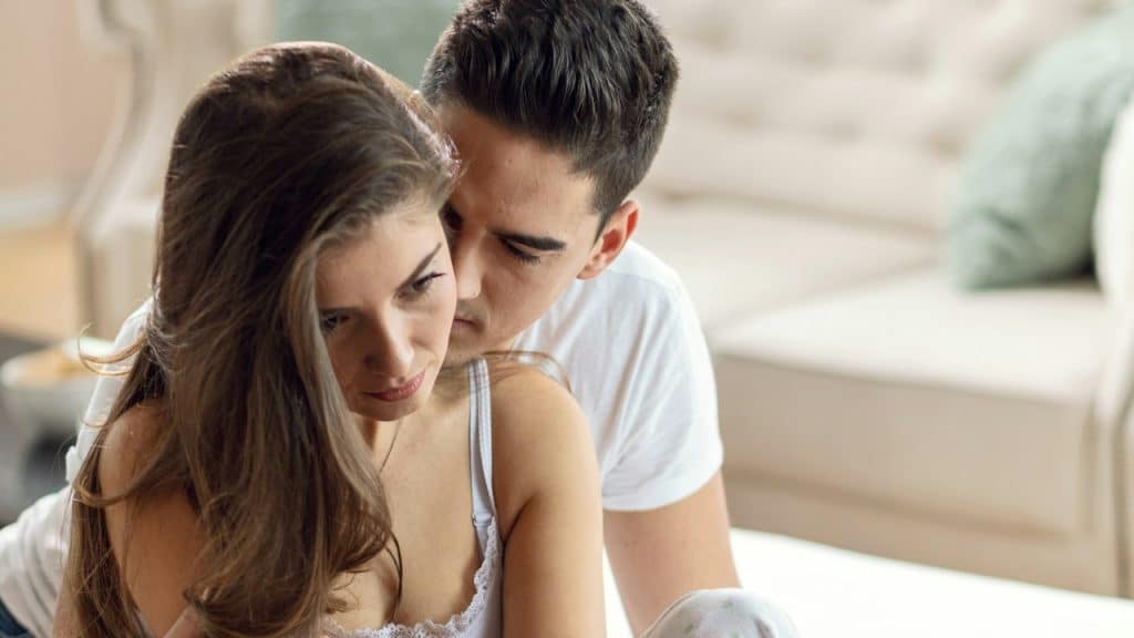A young woman is feeling sad while her husband is embracing her.