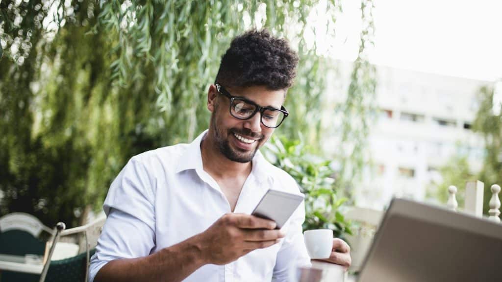 A young man smiling while reading texts from a social media friend.