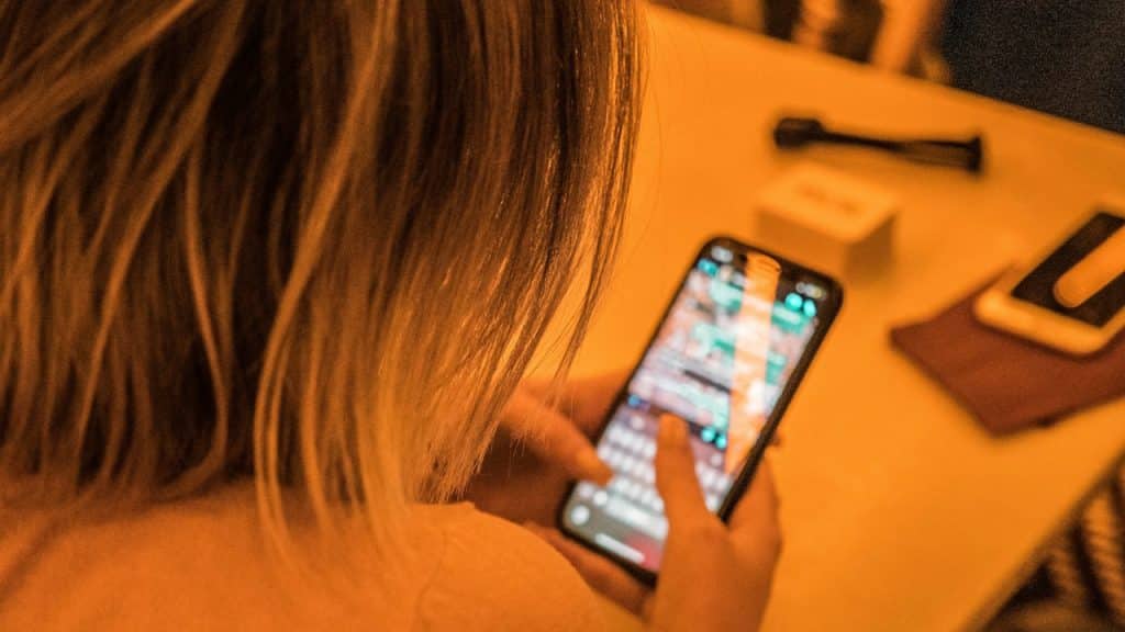 Over-the-shoulder view of a person with blonde hair looking down and typing on a smartphone.