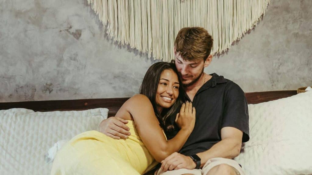 A couple cuddling on a bed and smiling warmly.
