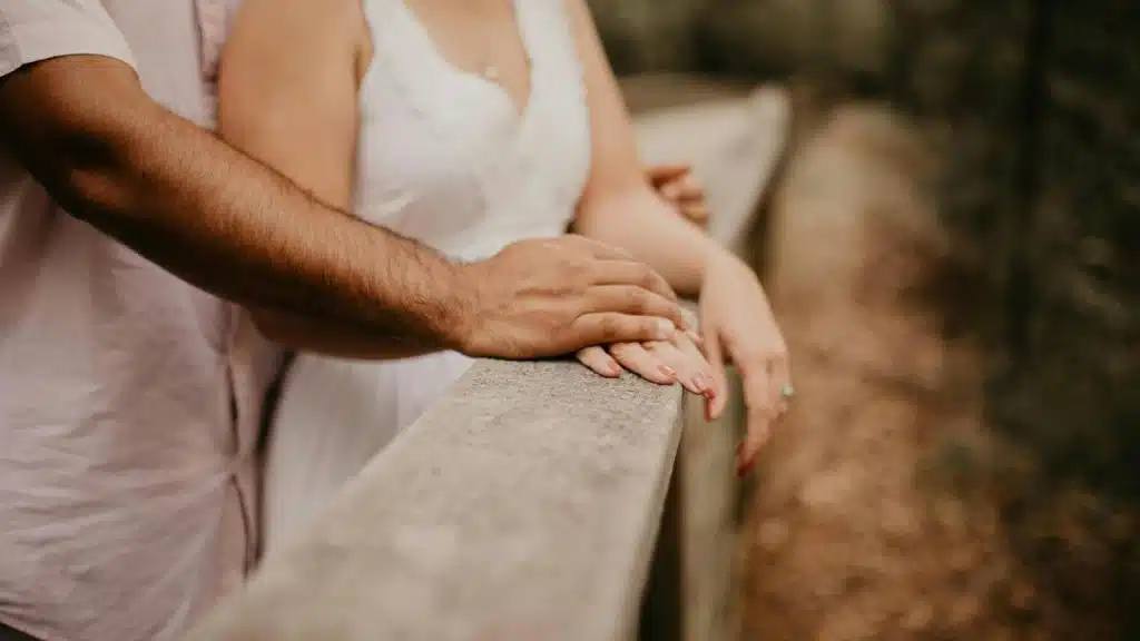 A couple stands close together with their hands resting on a railing.