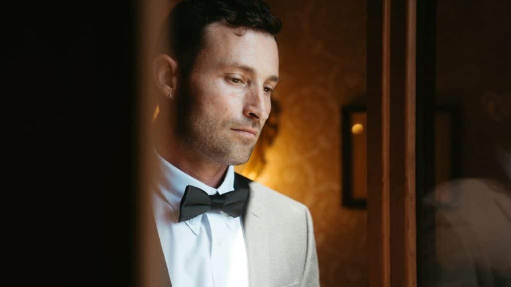 A man in a suit and bow tie is looking down with a serious expression.