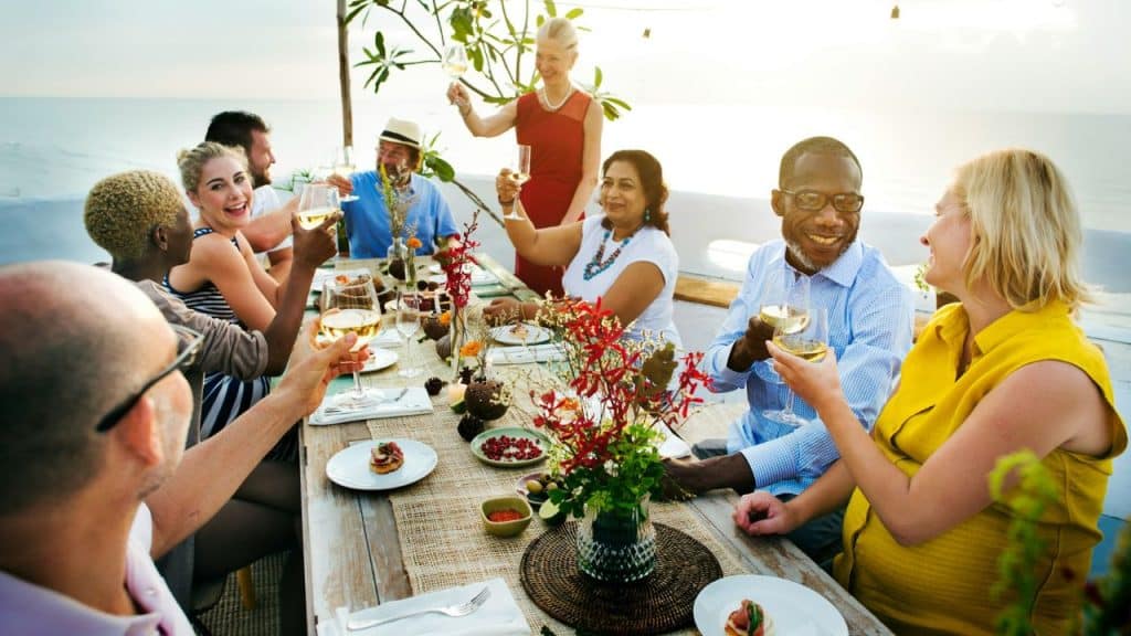Diverse group of people smiling and toasting with wine glasses at an outdoor table.
