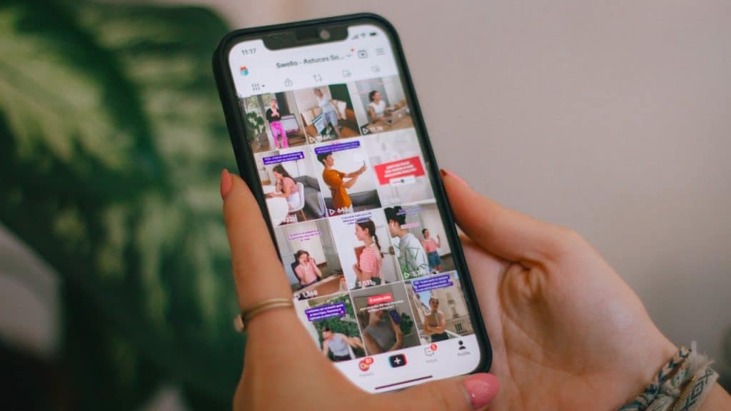 Two hands hold a smartphone displaying a grid of short videos on a social media app.