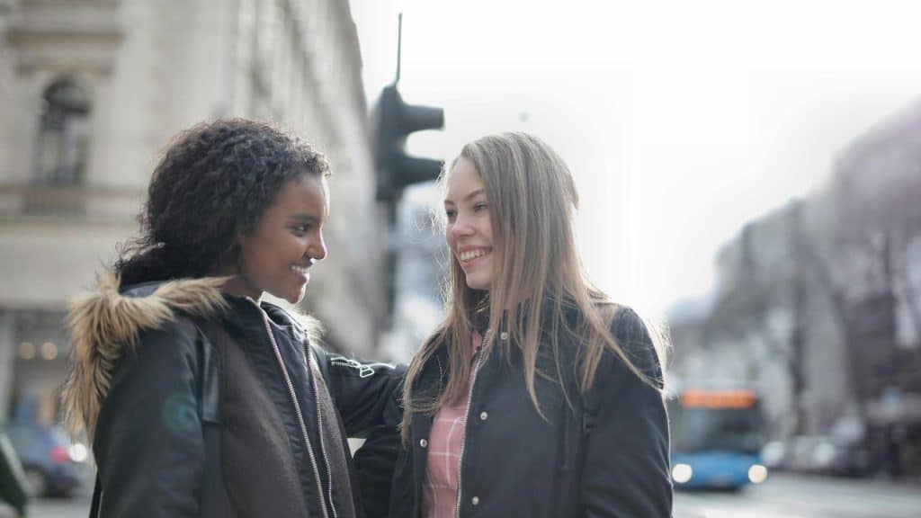 A pair of friends smiling and talking together on a city street.