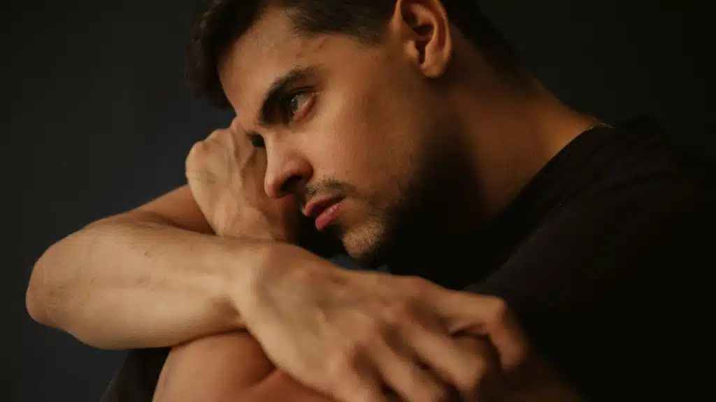 Man resting his head on his arms, looking off to the side with a serious or pensive expression.