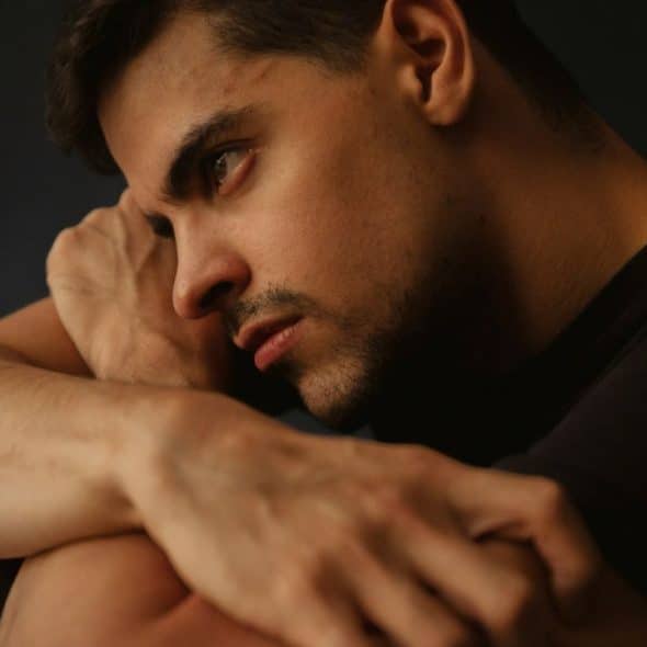 Man resting his head on his arms, looking off to the side with a serious or pensive expression.