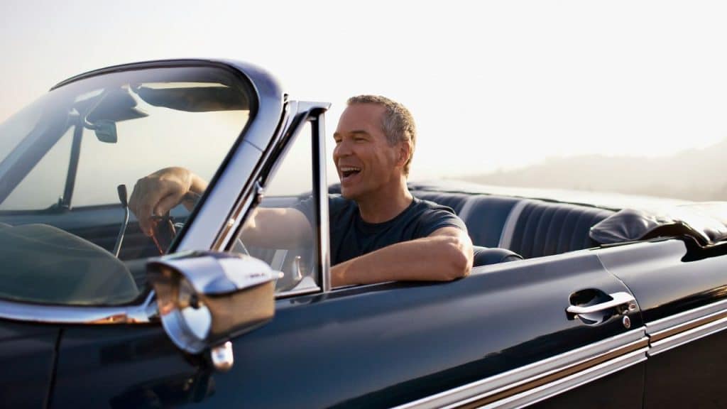 A joyful, middle-aged man is driving a classic convertible in the sunshine.