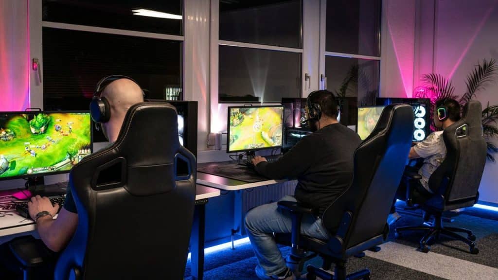 Three men with headphones are playing computer games in a room with neon light.