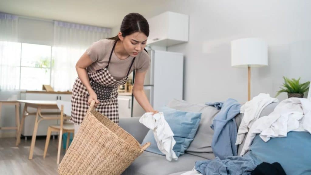 Woman picking up the dirty clothes on the couch to wash