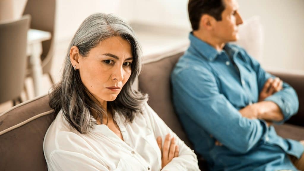 A couple in a fight keeping silent and sitting with their arms crossed on a couch.