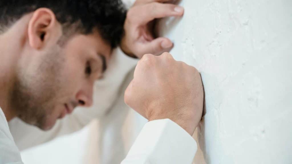 A man leaning against a wall with his fist pressed to it.