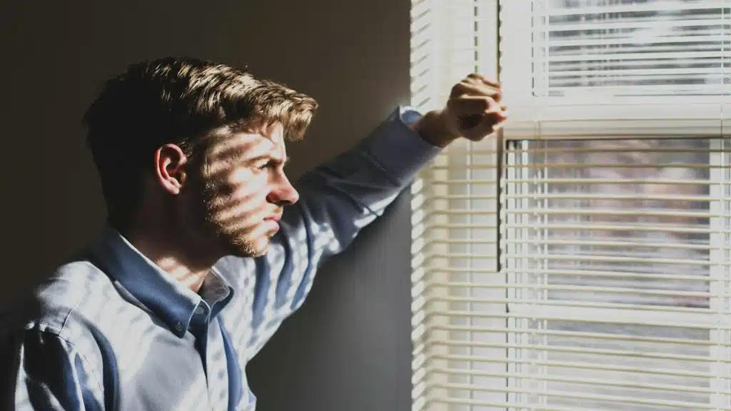 A sad man standing near the window.