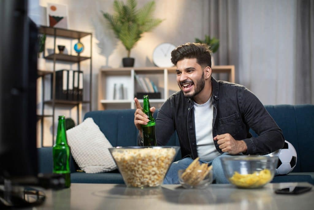 The man is holding a beer while watching TV.