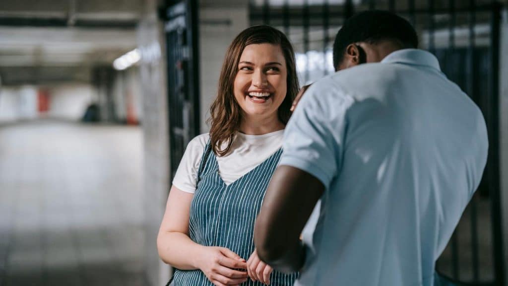A woman smiling while talking to a man in a hallway.