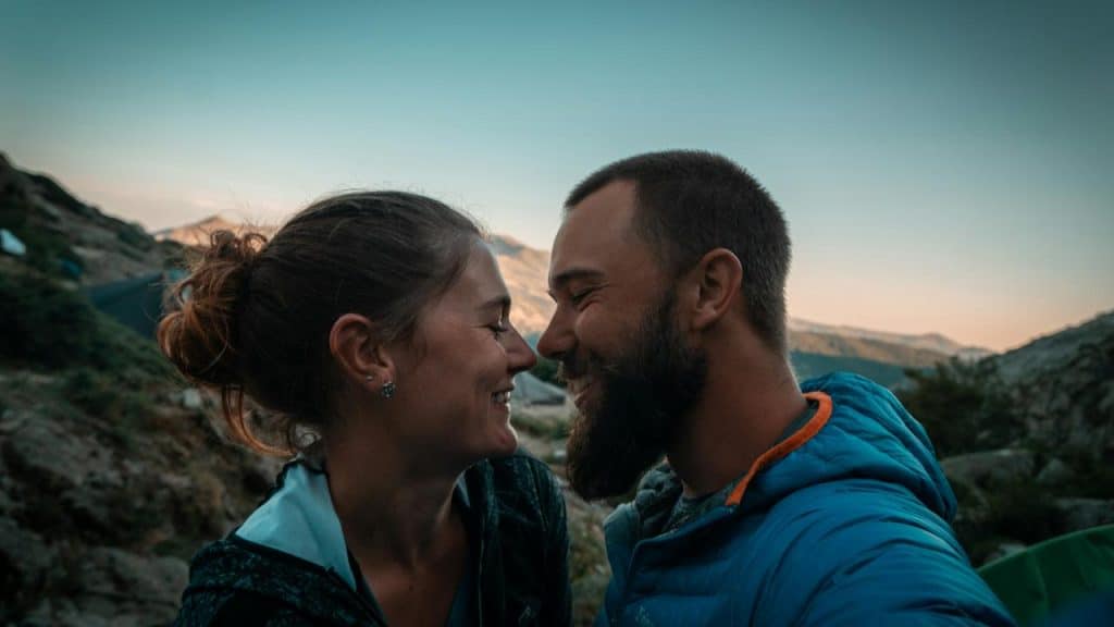 A couple smiling closely at each other while camping in the mountains.