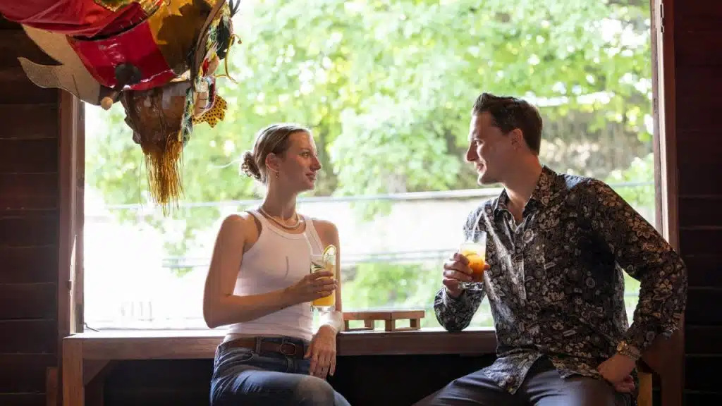 Man and woman sitting by a window, facing each other and holding drinks.