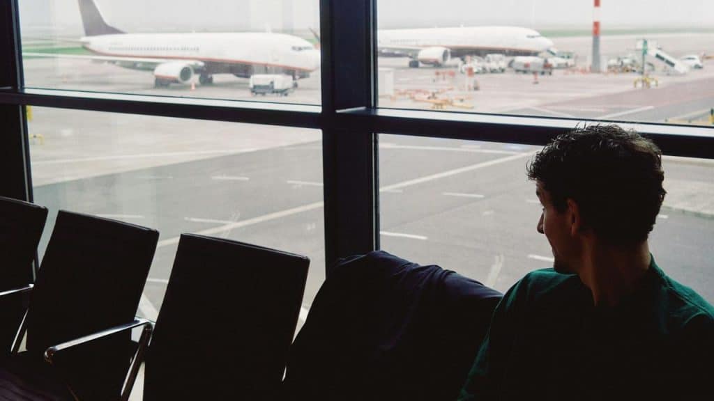 A man sitting in an airport terminal looking at planes outside.