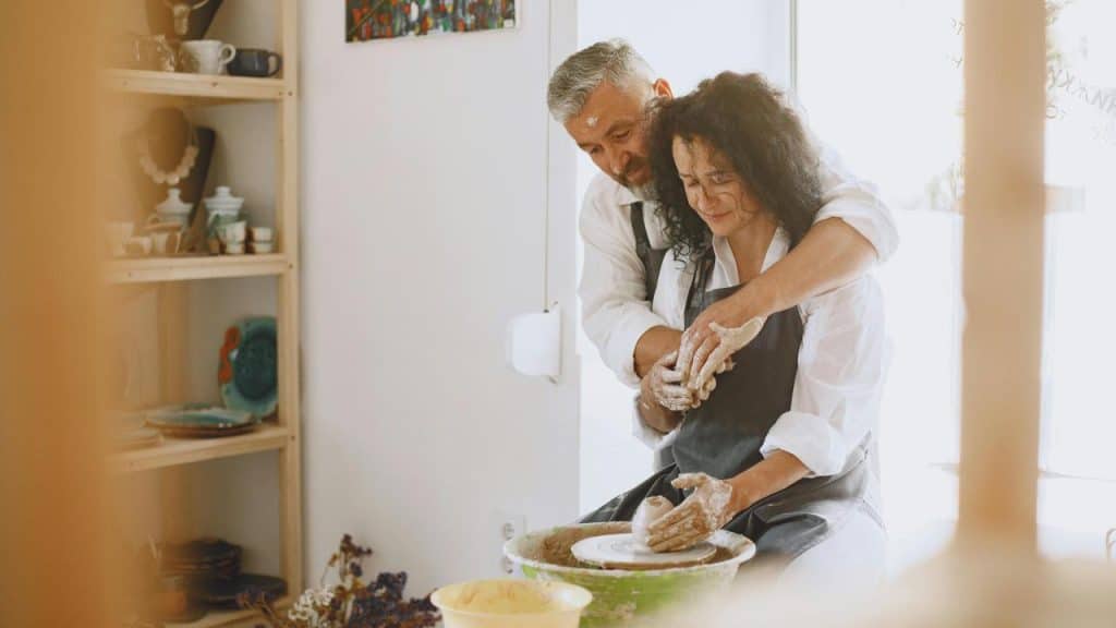 A couple happily working together on pottery at a pottery wheel.