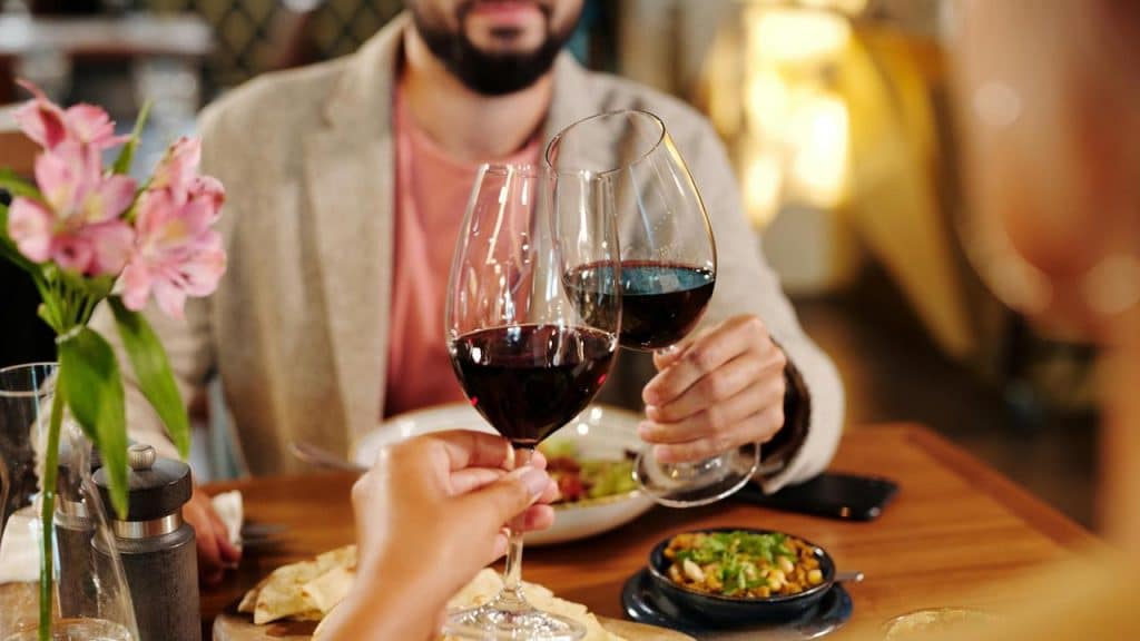 A couple clinking glasses of red wine at a restaurant table.