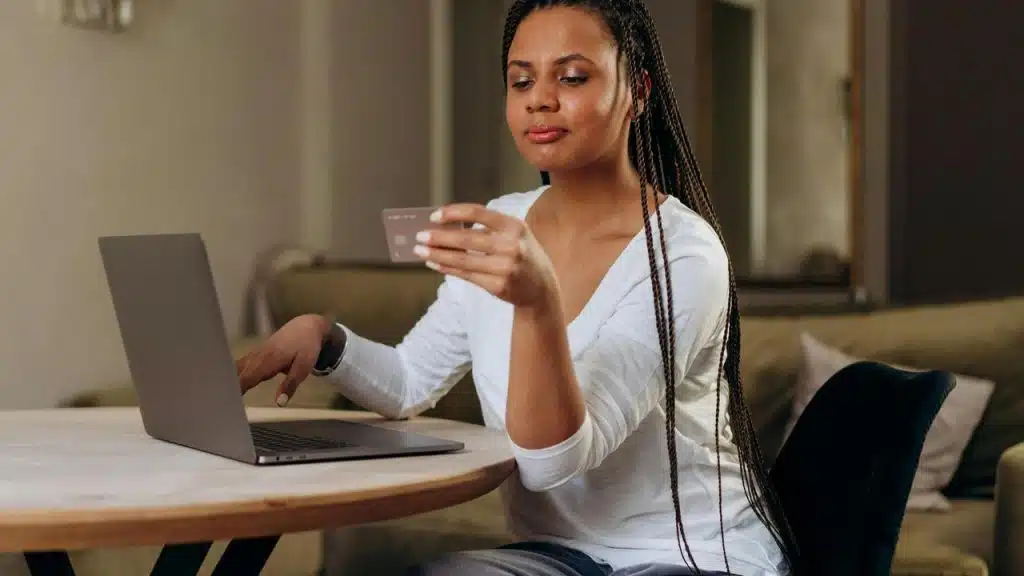 A woman holding a credit card while using a laptop at a table.